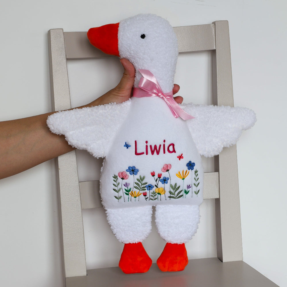White plush toy with red feet and beak, featuring colorful flowers and the name 'Liwia' on a white chair.