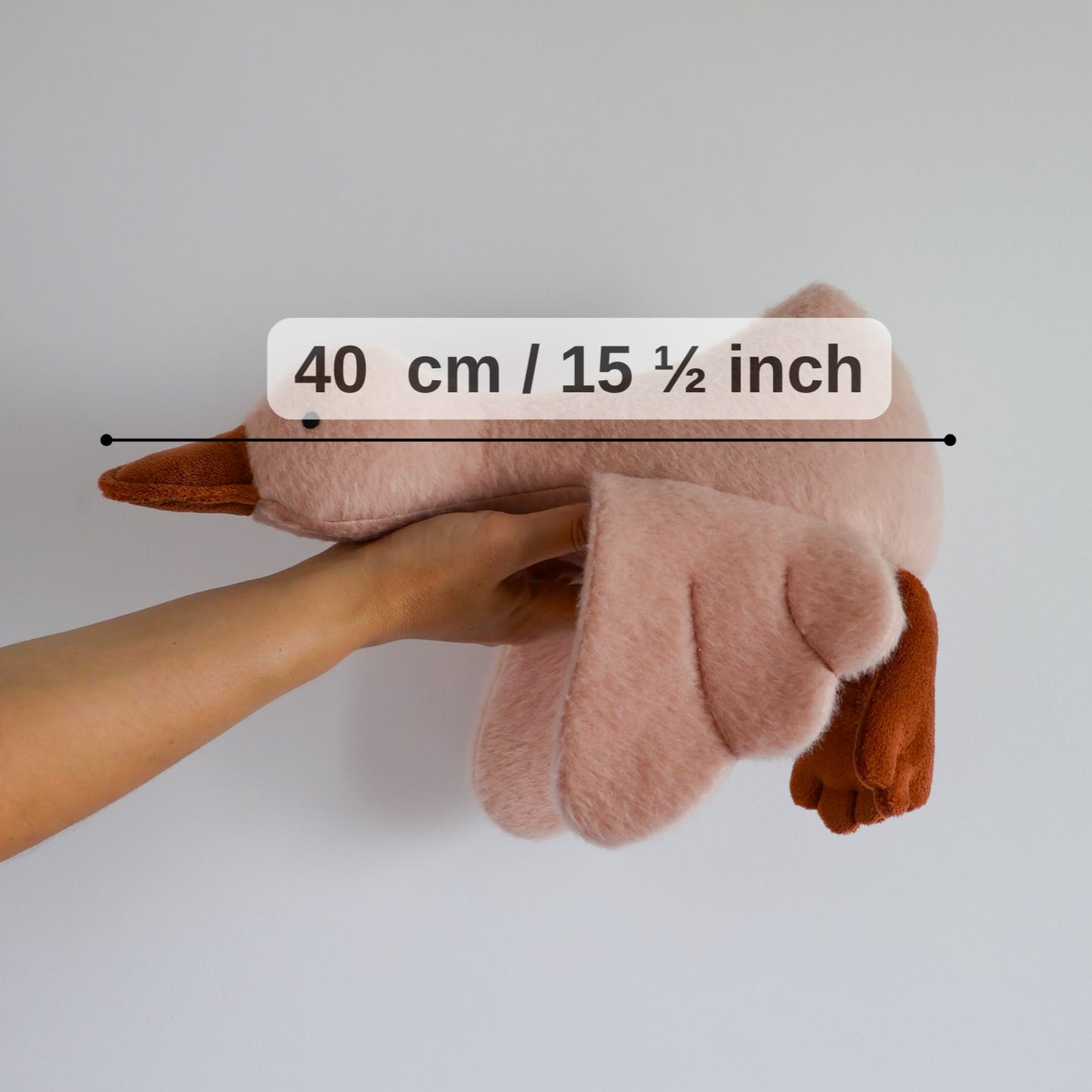 Hand holding a small plush toy with measurement label on a plain background