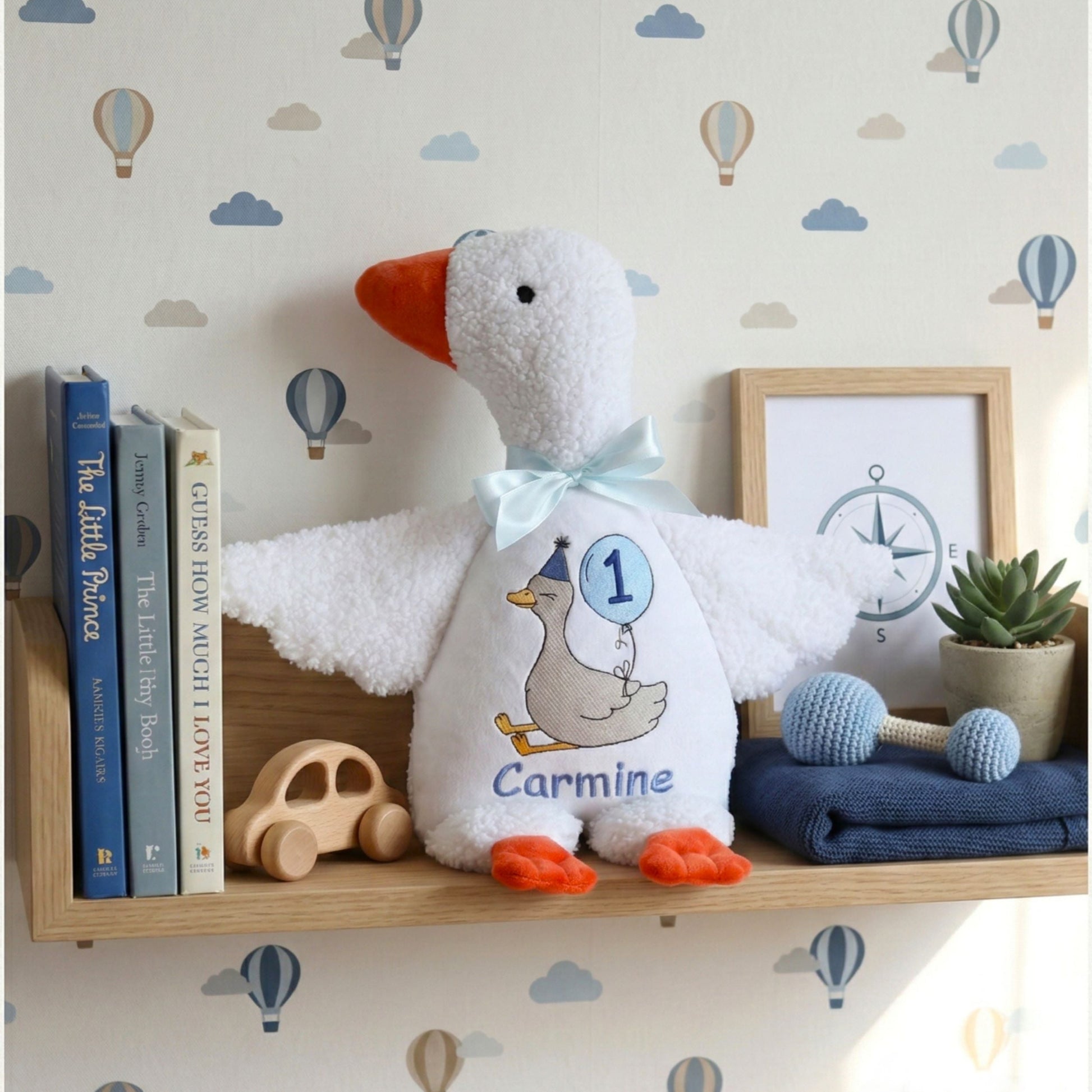 Hands holding a personalized baby boy plush goose milestone gift. Custom embroidered silly goose stuffed animal with name and age