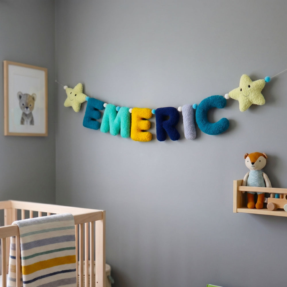 Children's room with a name banner on a gray wall, next to a crib and shelf with toys.
