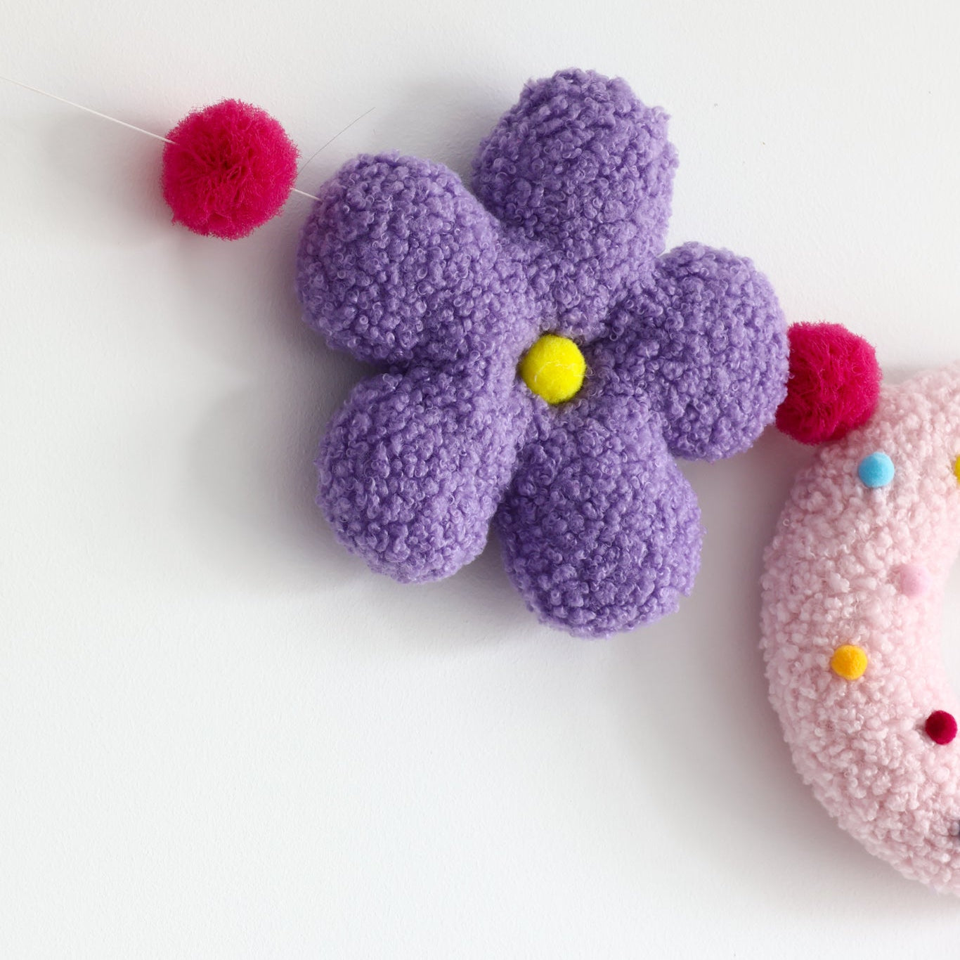Purple flower-shaped object with colorful pom-poms on a white background