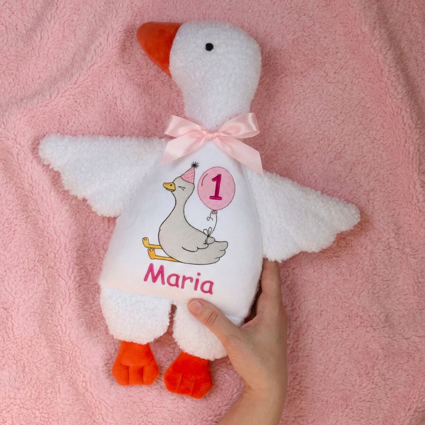 White plush duck toy with pink bow and personalized design on a pink blanket