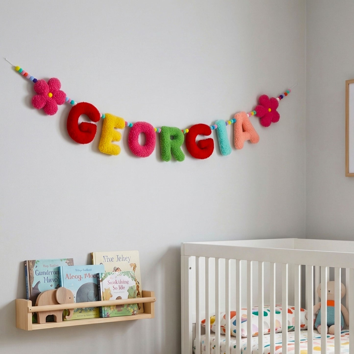 Colorful 'GEORGIA' banner above a crib with books and toys in a nursery.