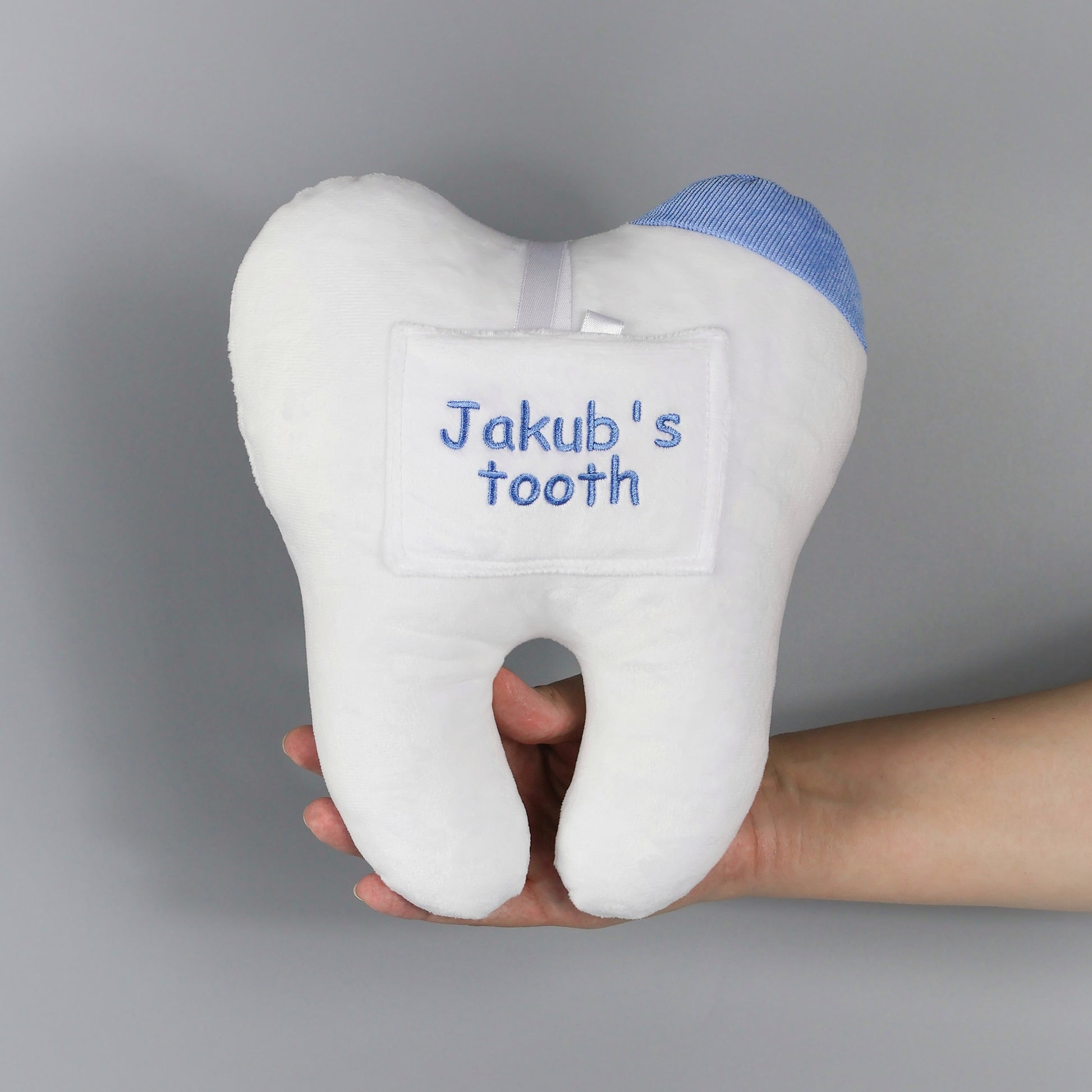 White tooth fairy pillow with blue text 'Jakub's tooth' held by a hand 