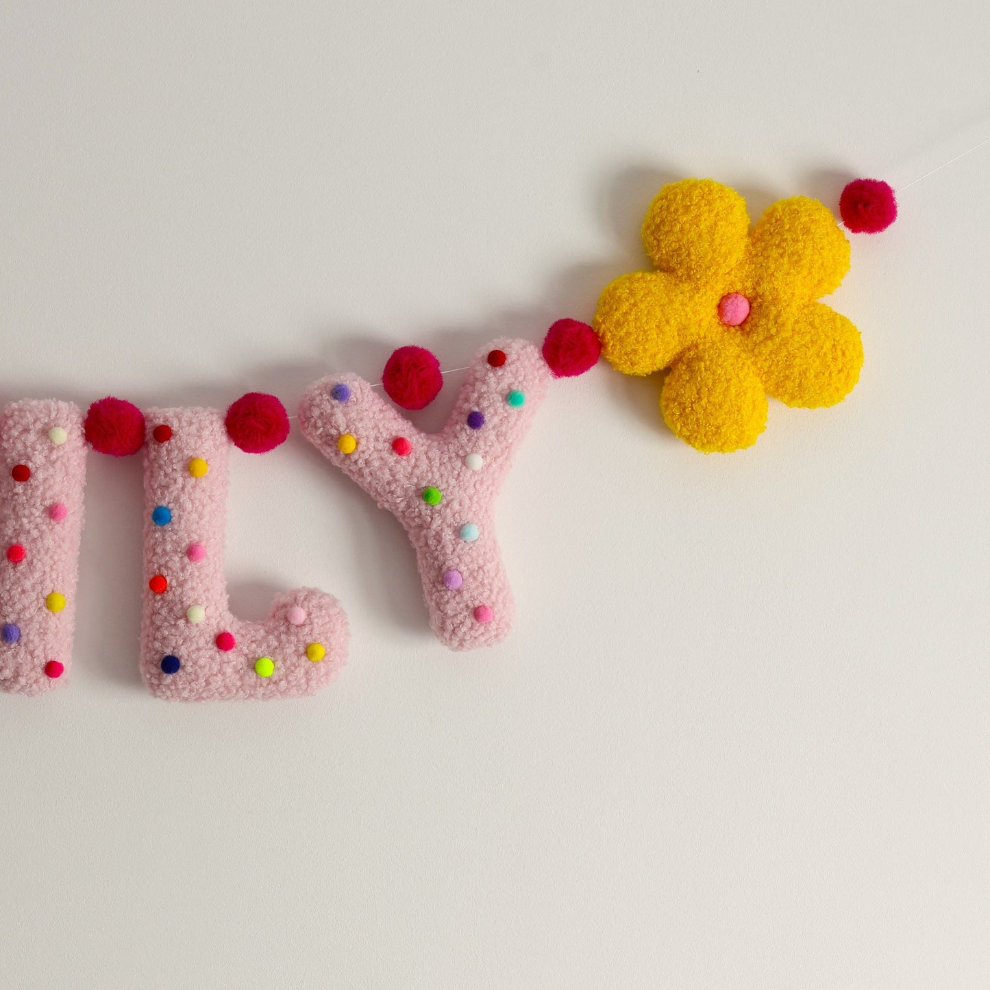 Decorative letters garland with colorful pom-poms and a yellow flower on a light background