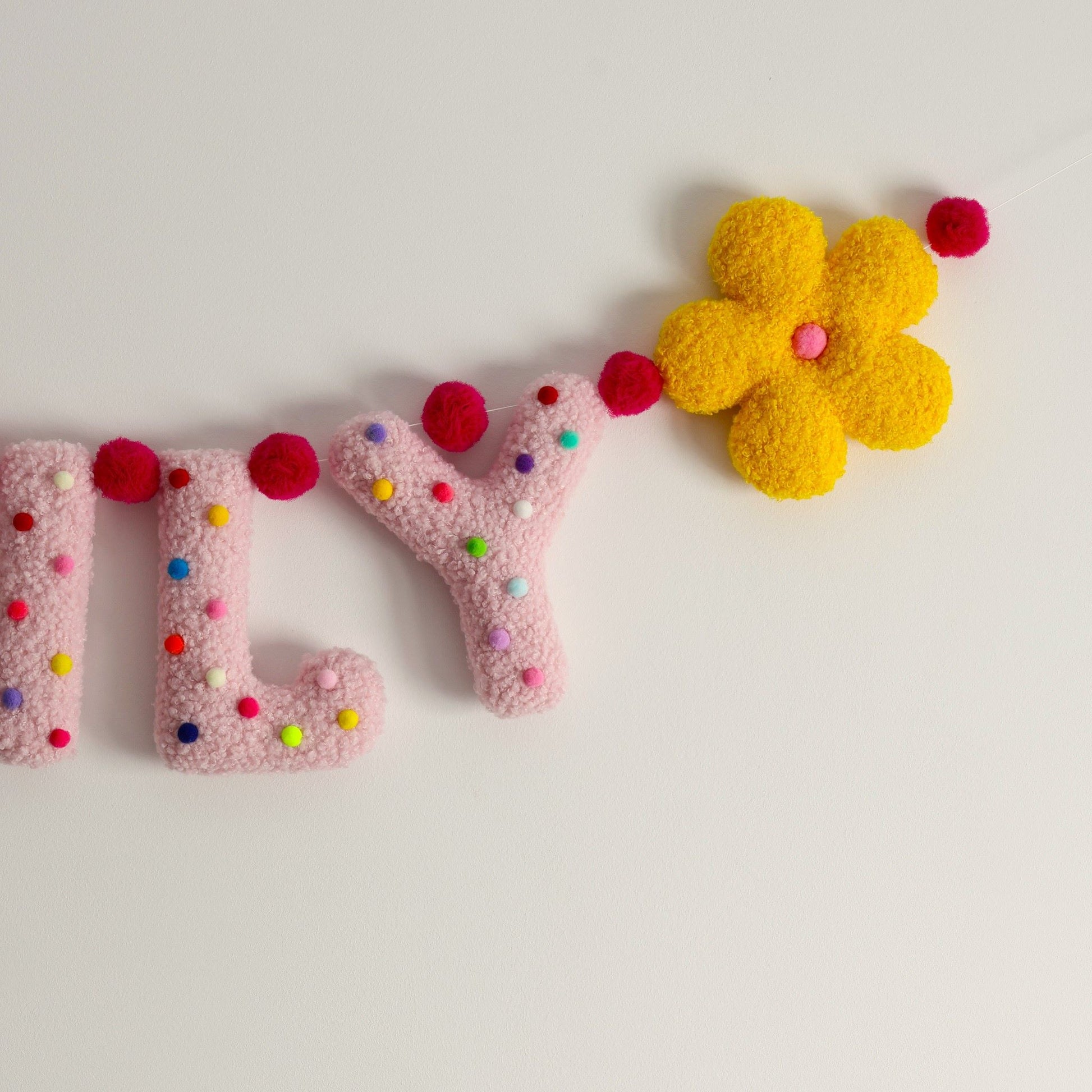 Decorative letters garland with colorful pom-poms and a yellow flower on a light background