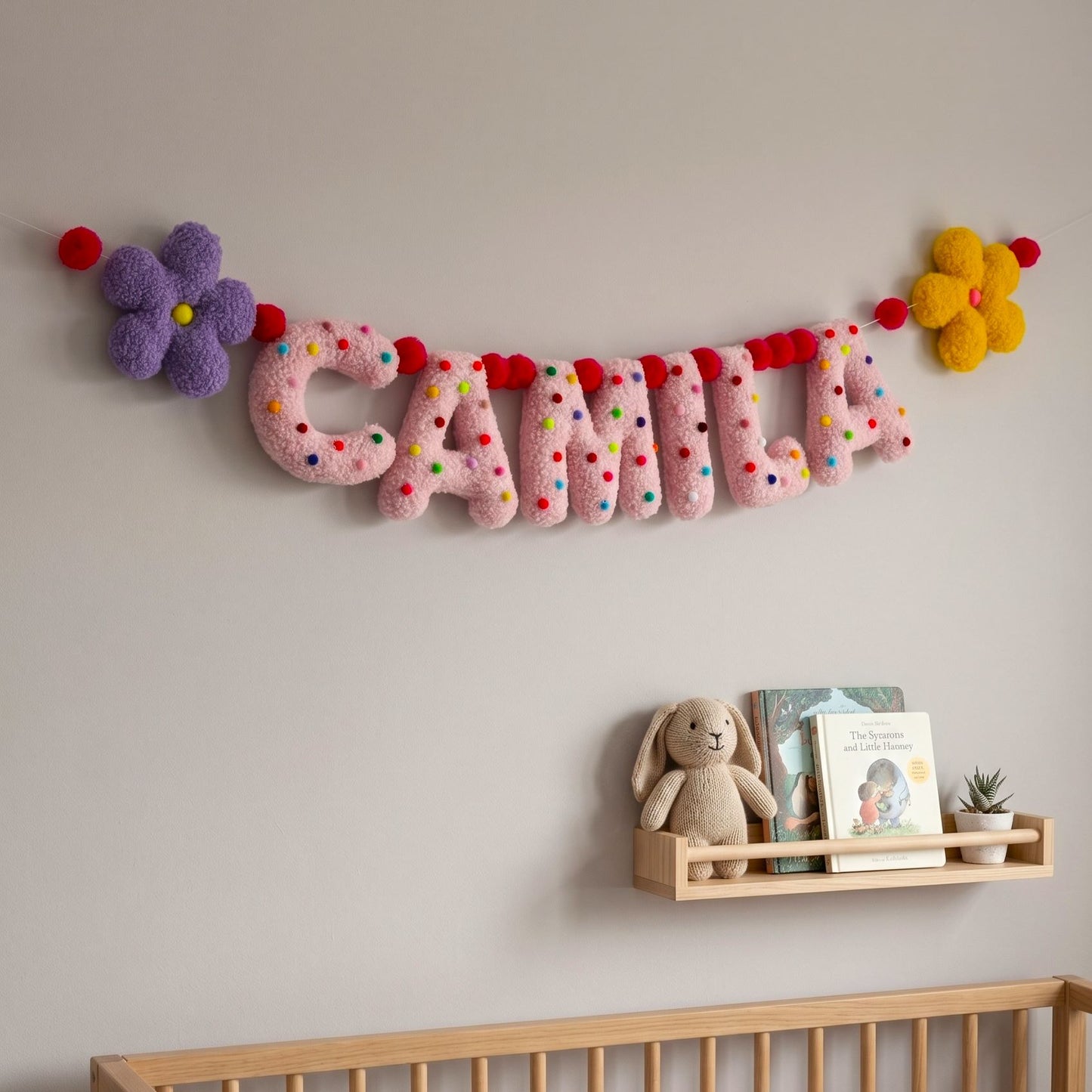 Decorative name banner with colorful letters on a wall above a shelf with a teddy bear and books.