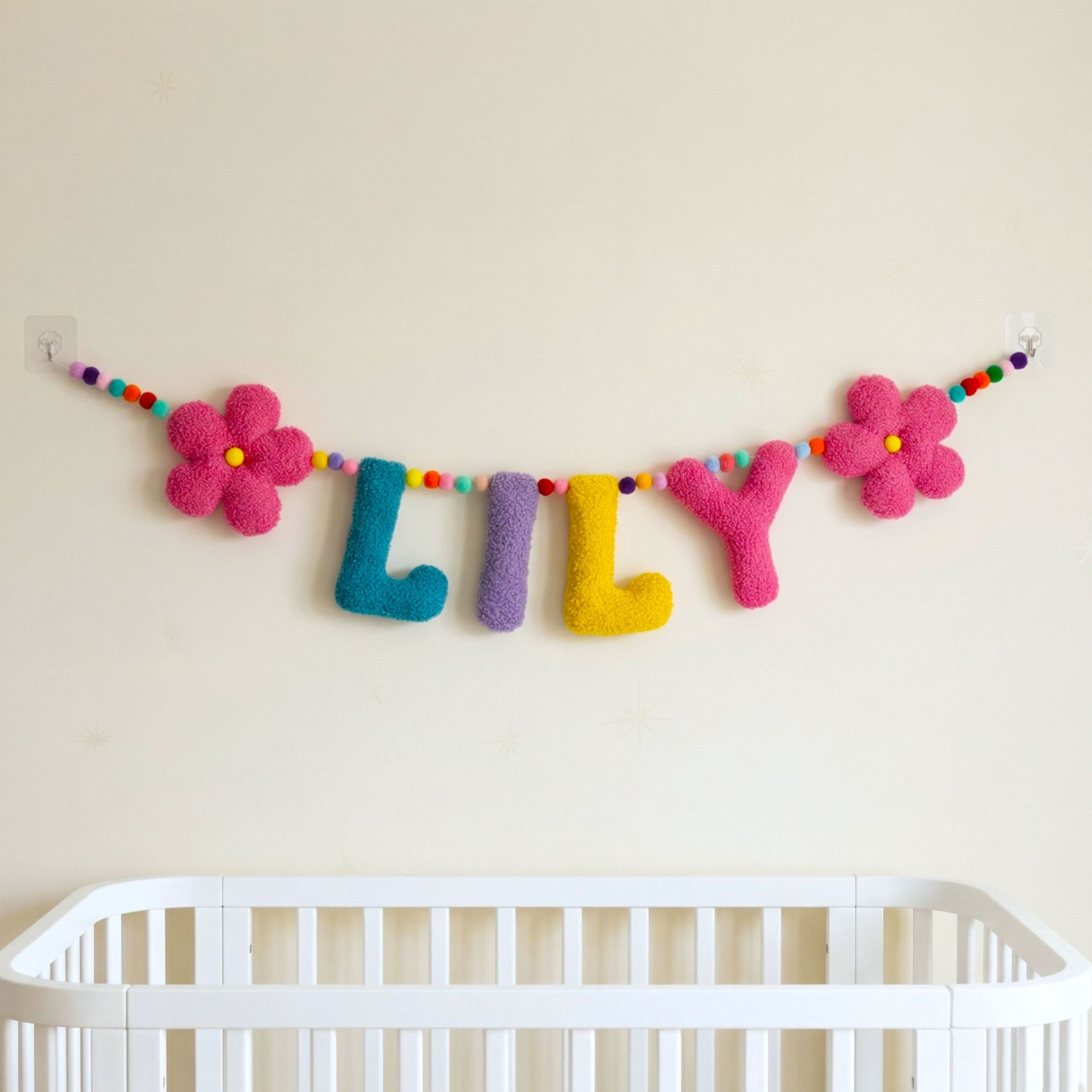 Colorful 'LILLY' name banner above a crib on a beige wall