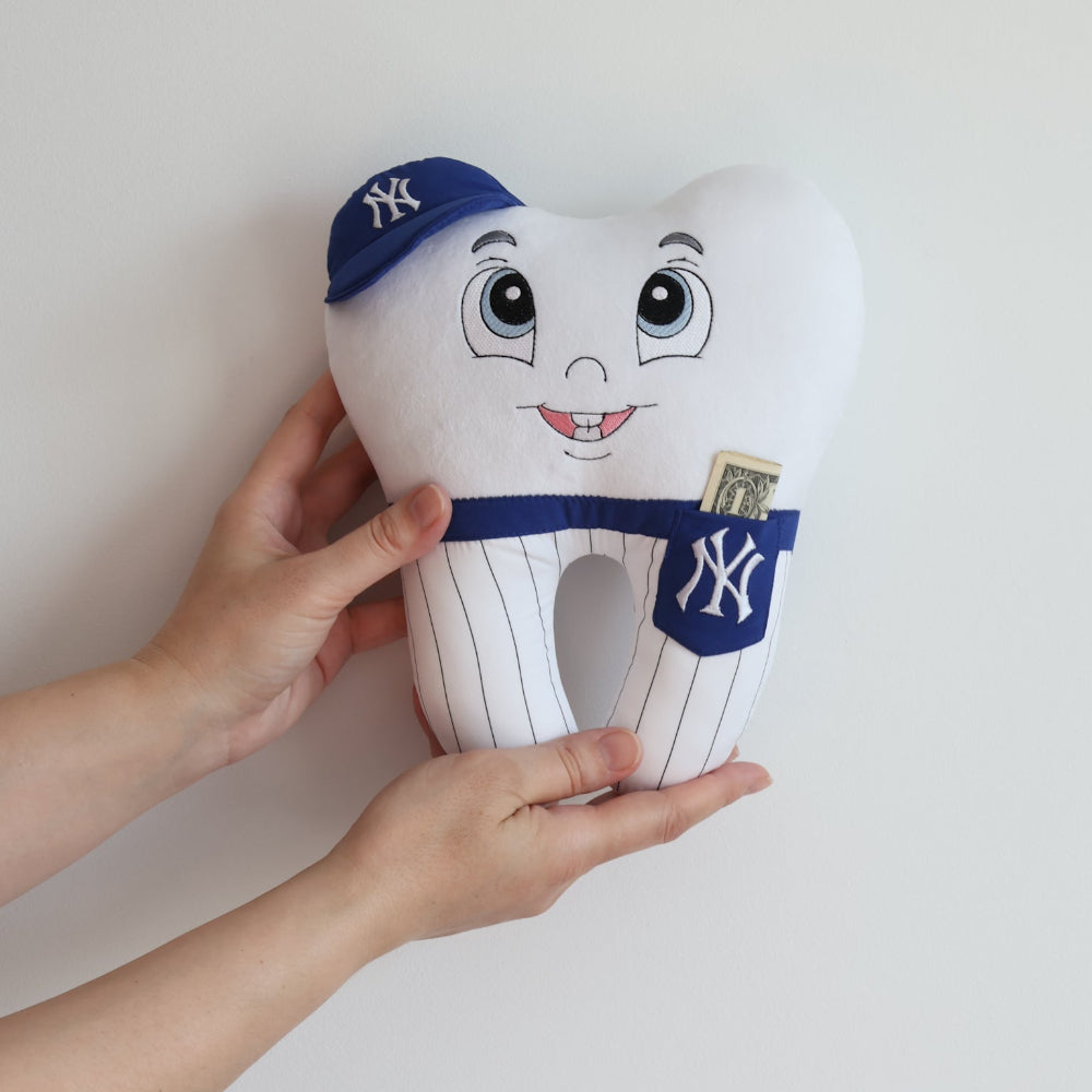 Toy tooth with a face, blue cap, and striped uniform held by a hand against a white background
