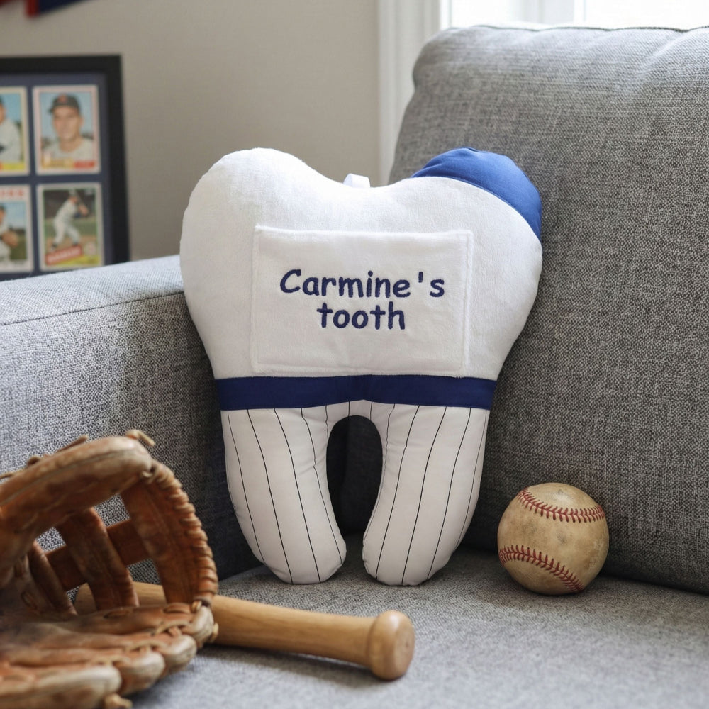 The back side of a personalized baseball tooth fairy pillow featuring custom computer embroidery that reads Carmine's tooth on a soft white plush background.