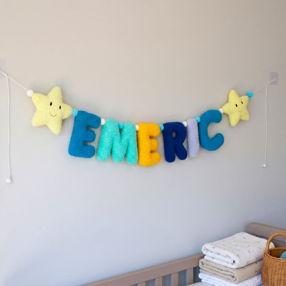 Colorful name banner with star decorations on a wall above a crib.