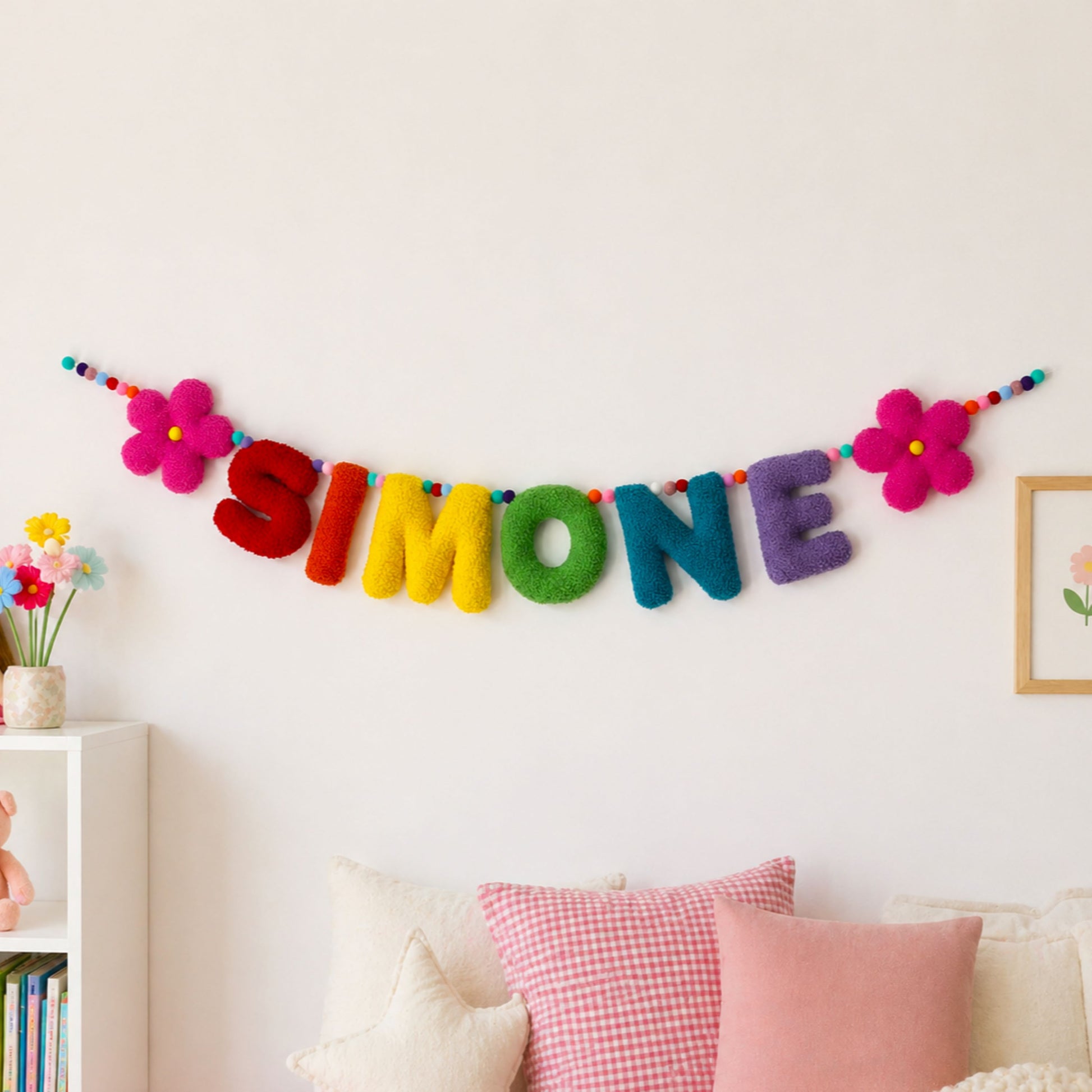 Colorful 'SIMONE' name banner on a wall with decorative pillows and flowers.