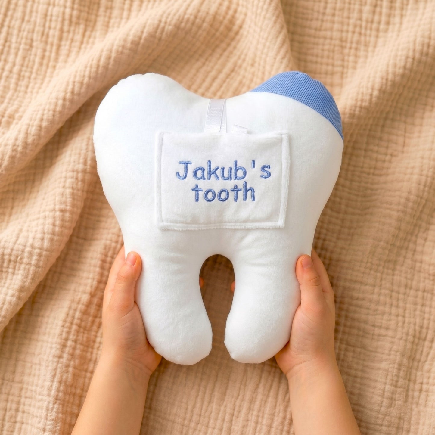 Plush tooth-shaped toy with 'Jakub's tooth' text held by hands on a beige fabric background