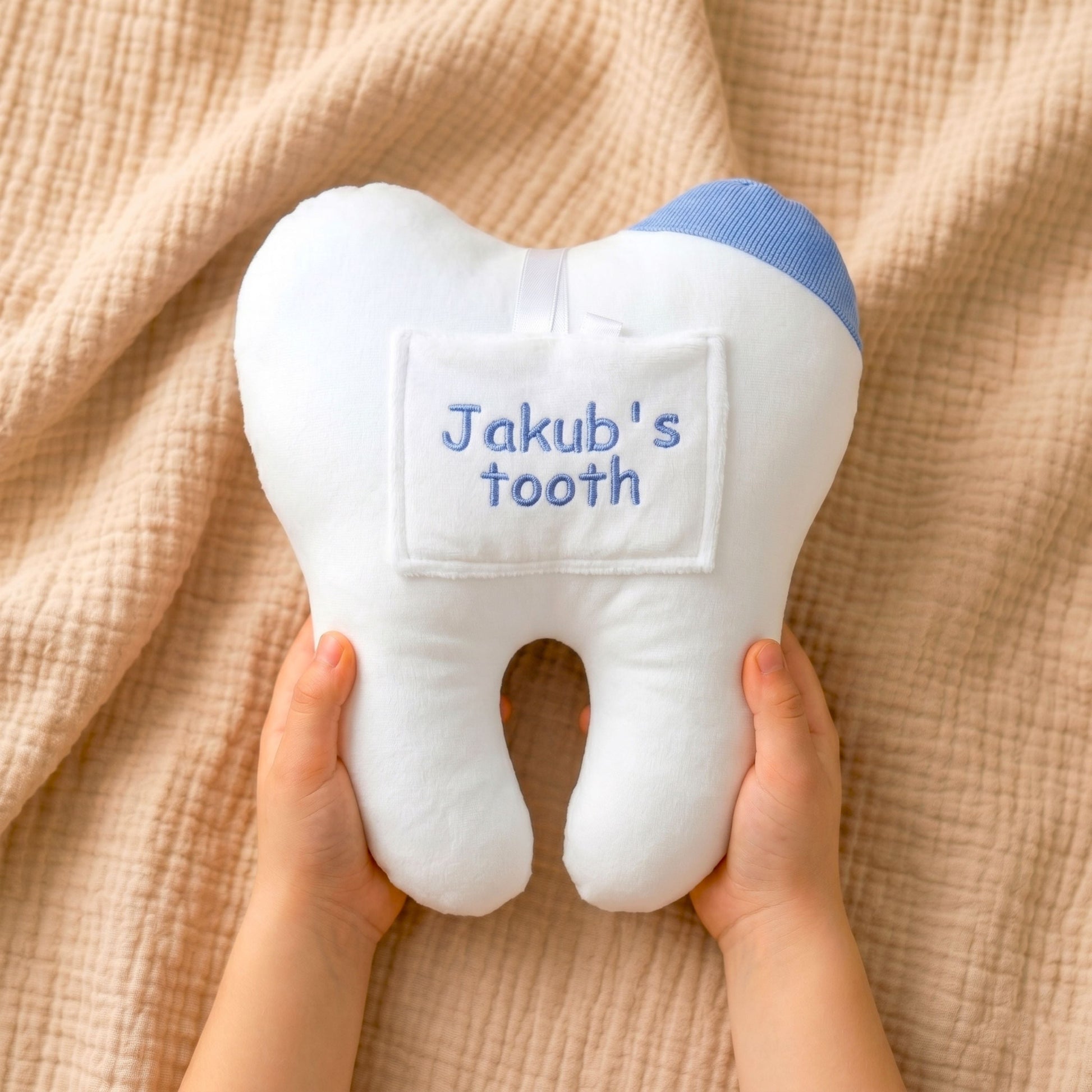 Plush tooth-shaped toy with 'Jakub's tooth' text held by hands on a beige fabric background