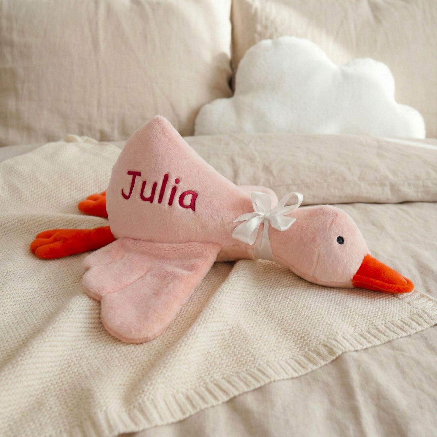 Pink plush duck toy with 'Julia' on a beige blanket