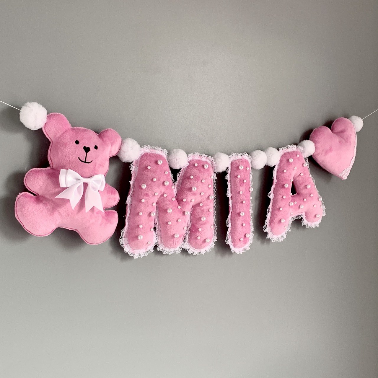 Pink personalized name banner MIA hanging above crib in baby girl nursery