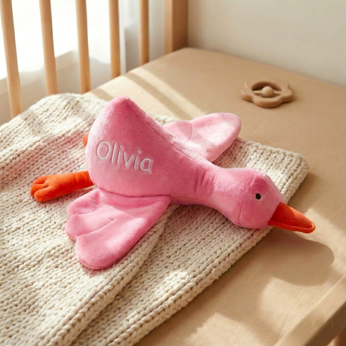 Pink plush duck toy with 'Olivia' on a crib