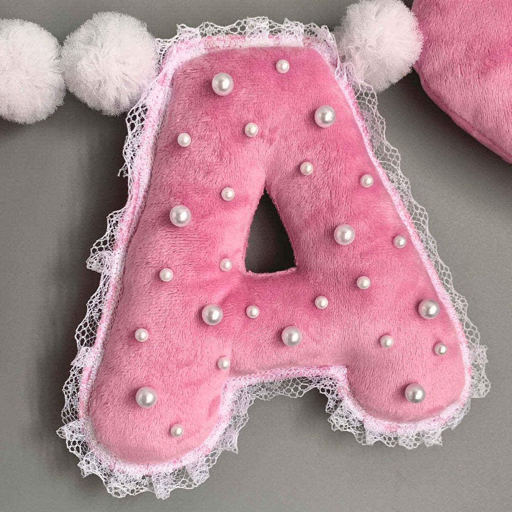 Pink plush letters with pearls and lace trim next to plush heart end piece