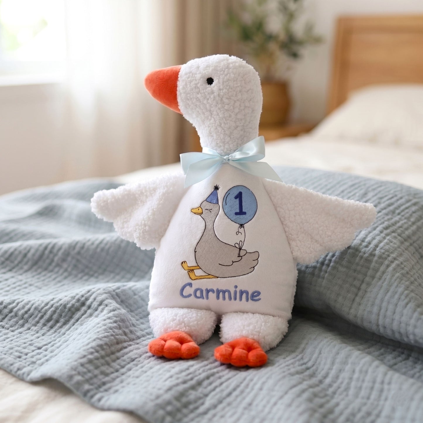 Plush toy goose with a bow and name on a bed