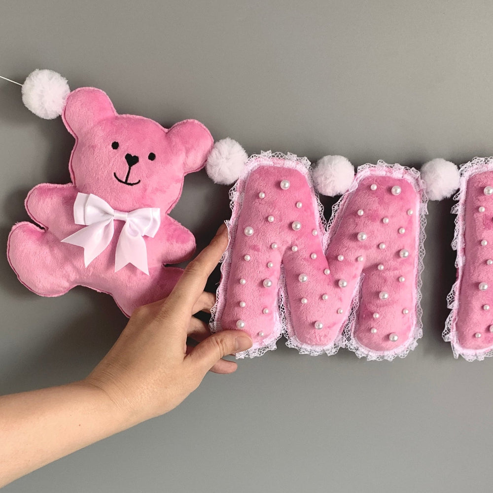 Close-up of handmade plush letters with pearl and lace detail, pink teddy bear accent