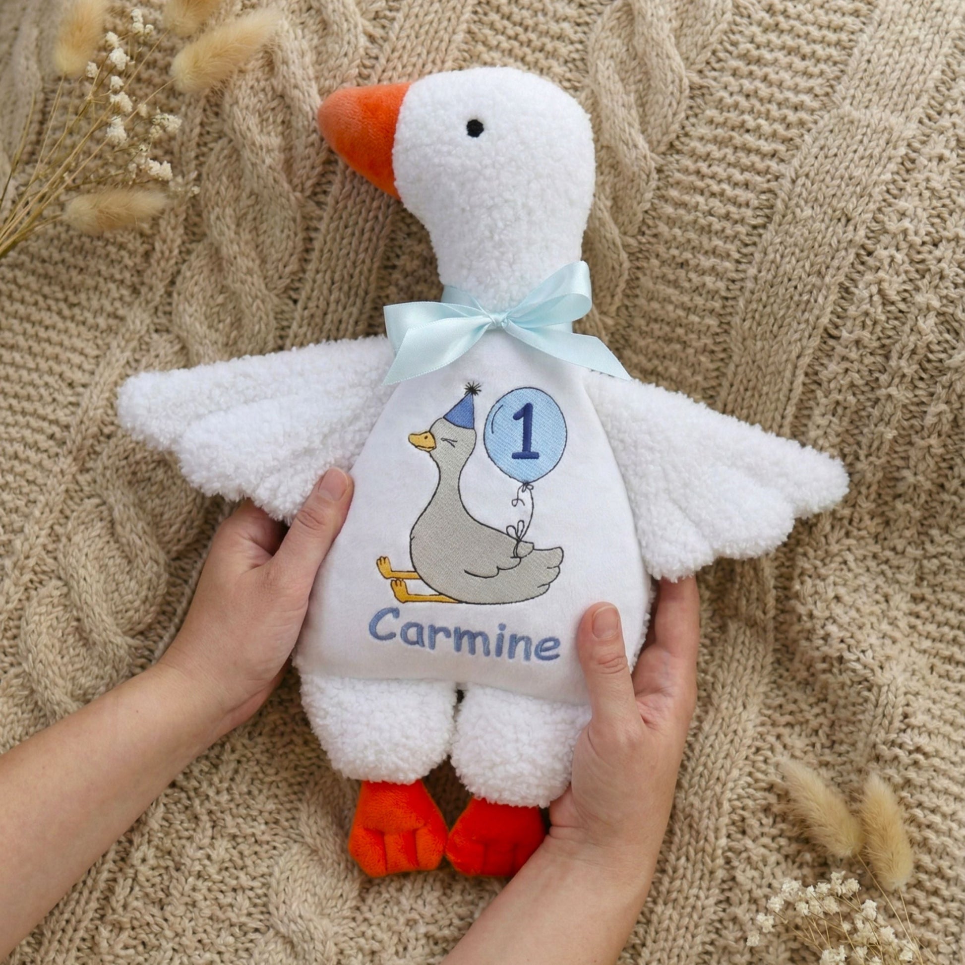 White plush toy goose with personalized details held by a person on a textured beige background