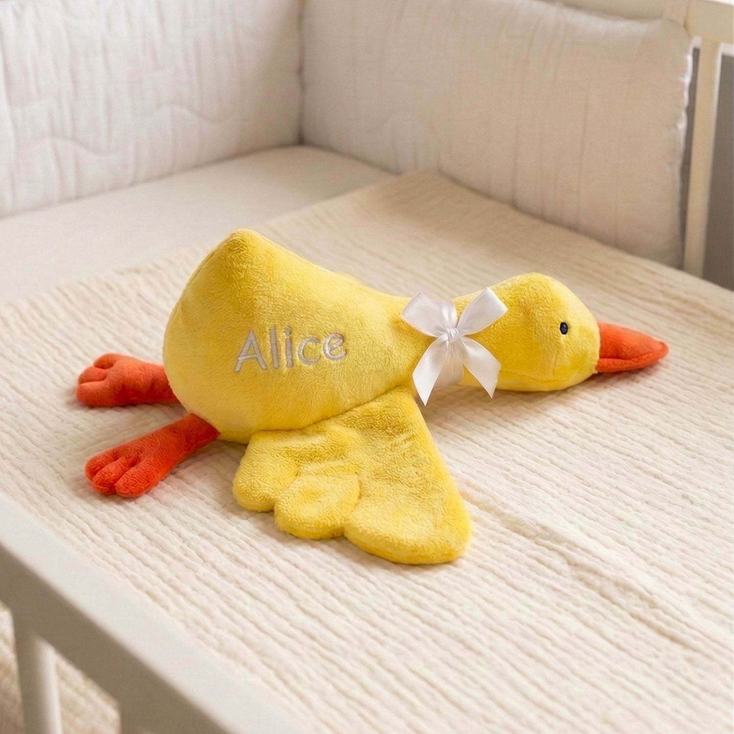 Yellow plush duck toy with a white bow and 'Alice' on a beige surface