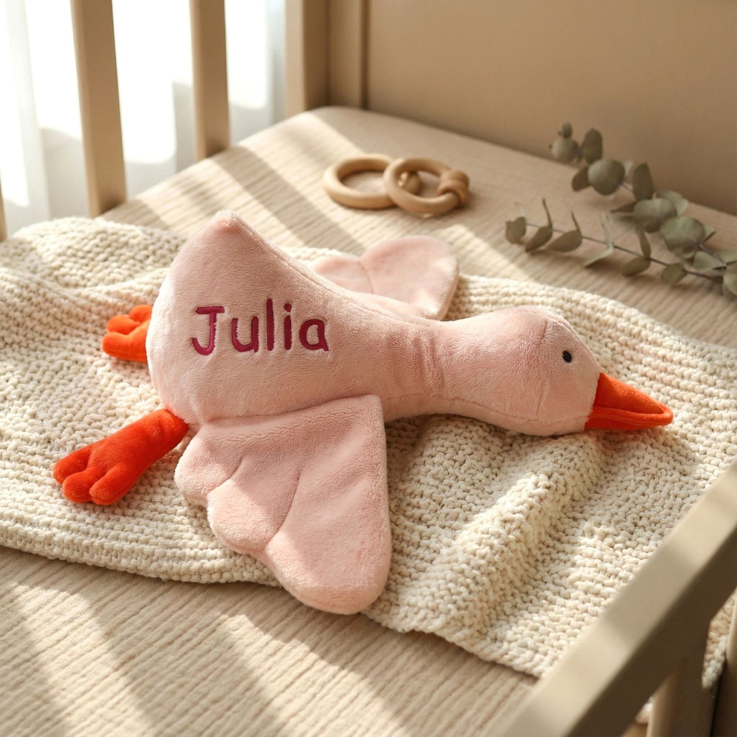 Pink plush duck toy with 'Julia' embroidered on it, placed on a textured surface.