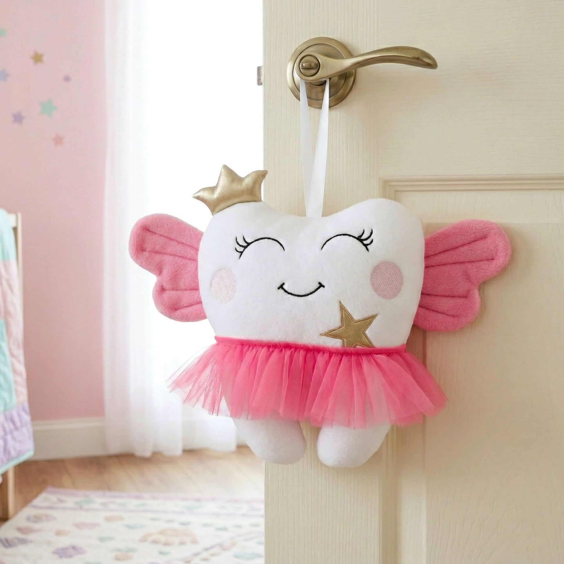 Plush tooth-shaped toy with wings and a crown hanging on a door handle in a child's room.