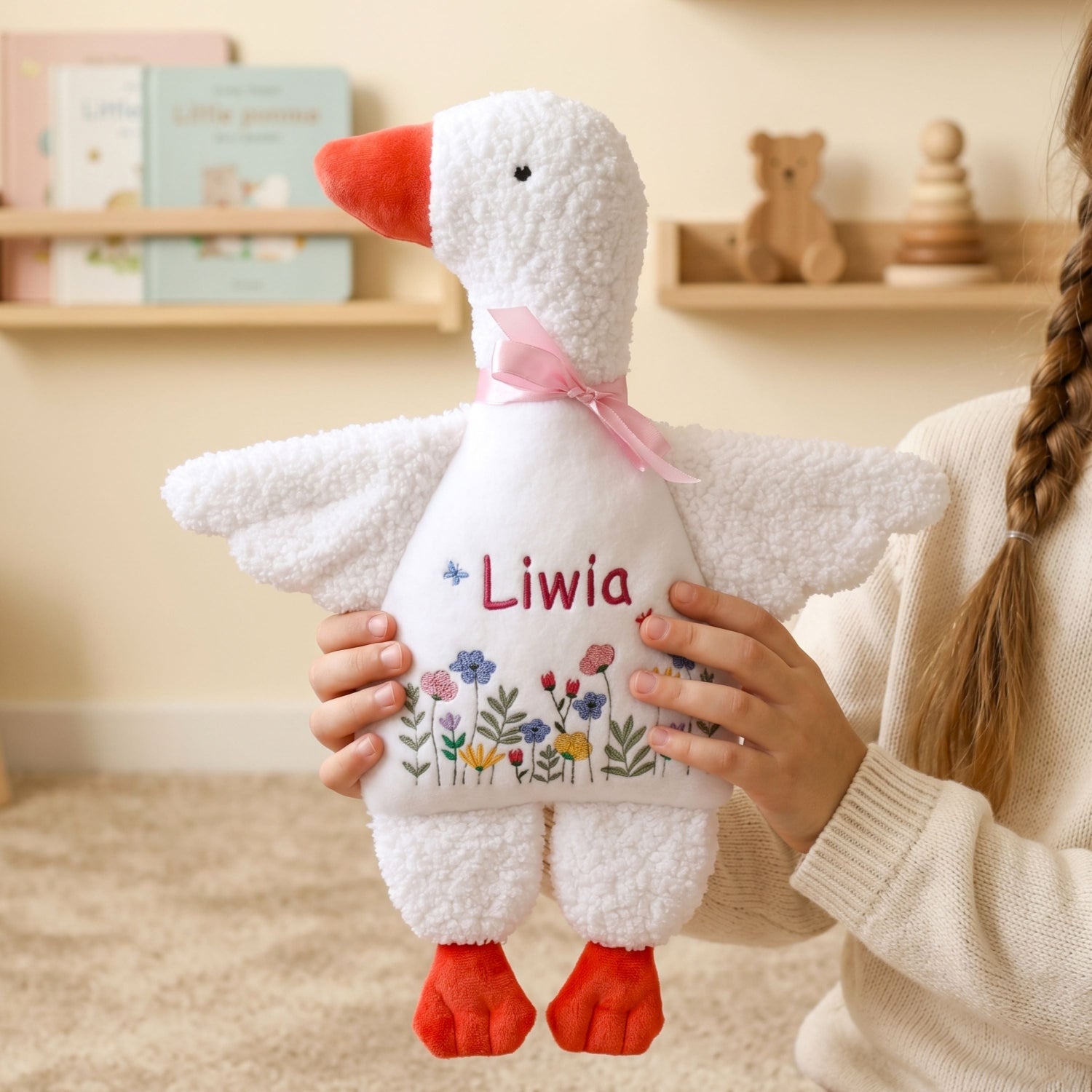 Child holding a plush toy goose with 'Liwa' embroidered on it, in a room setting.