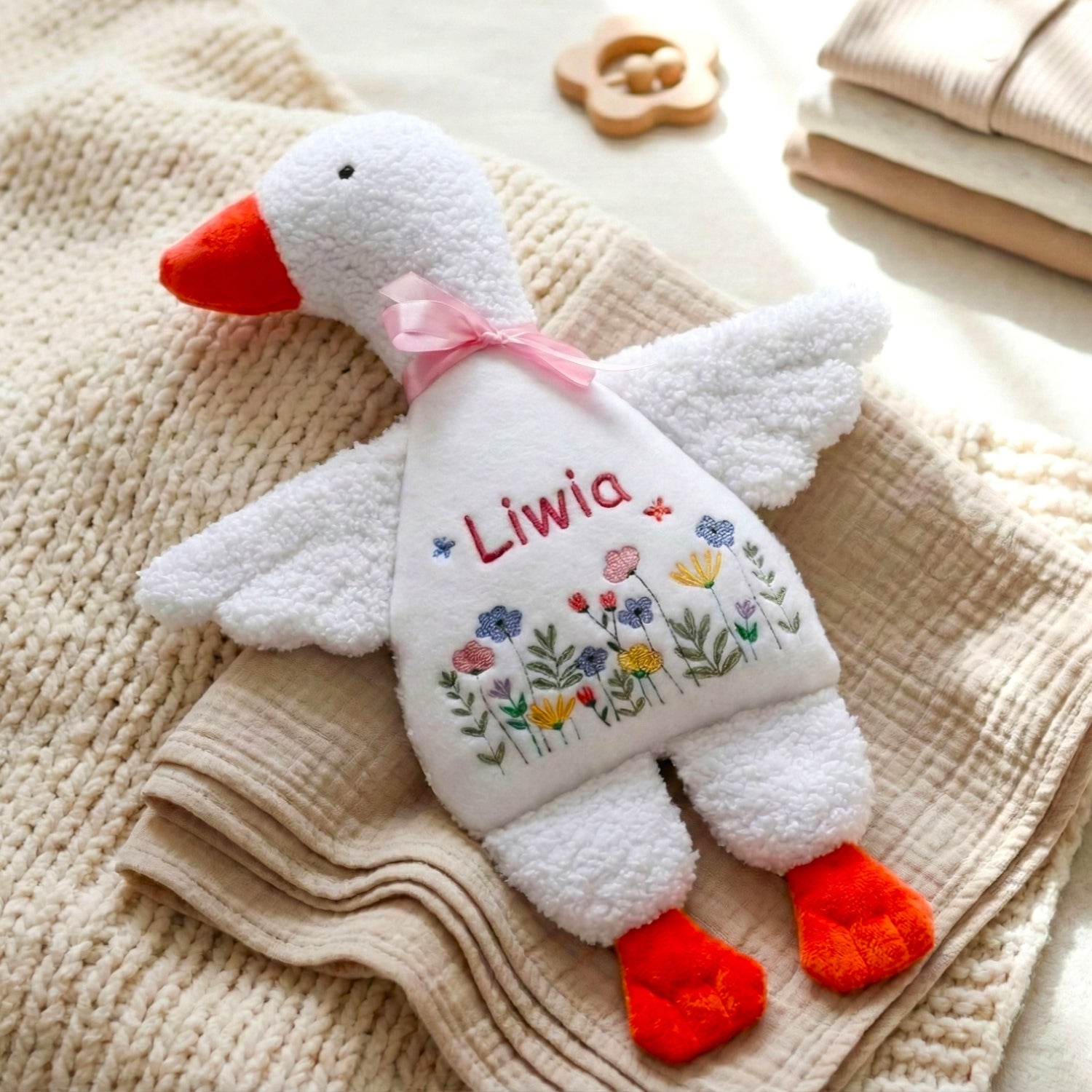 Plush toy goose with embroidered name and flowers on a textured surface