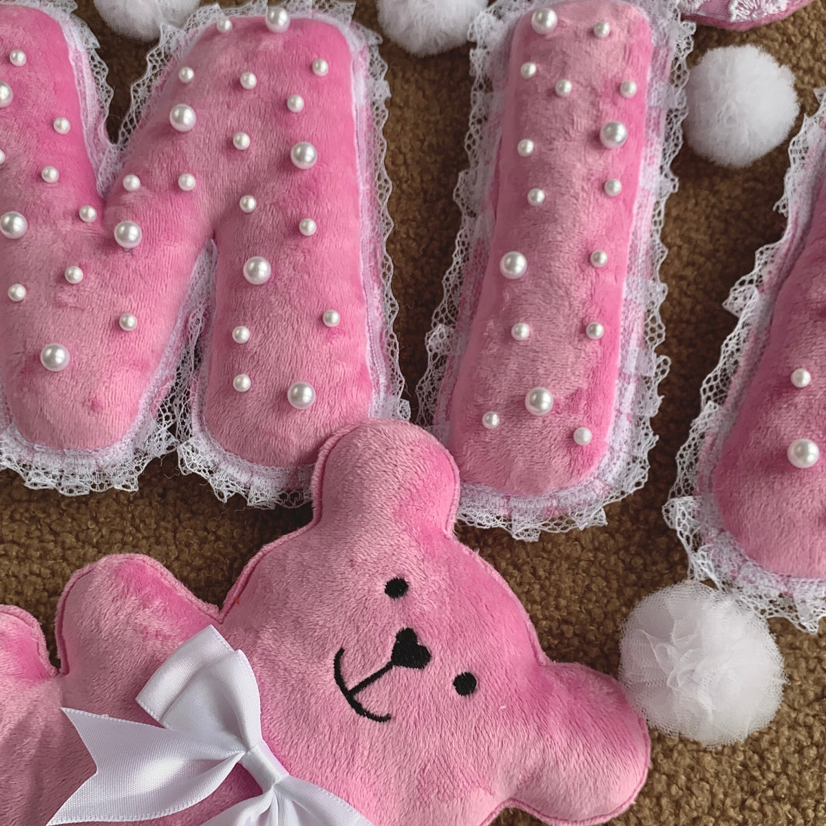 Macro detail of pink plush letter A with faux pearl embellishments and lace trim