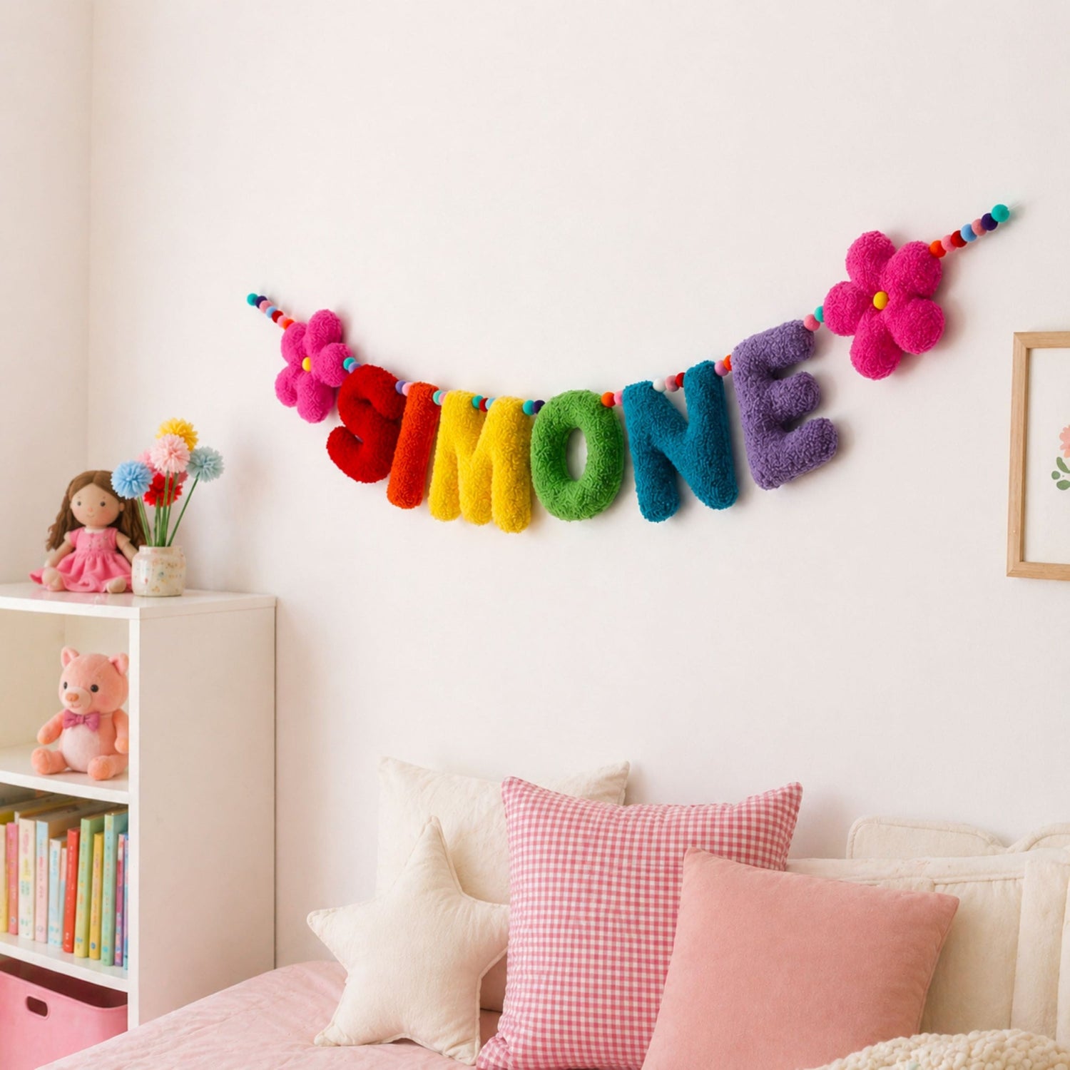 Colorful name banner on a wall above a bed with pillows and toys.