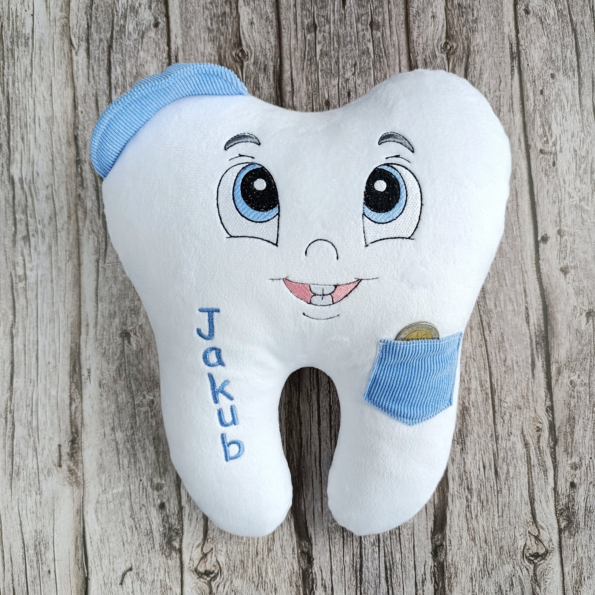 Plush tooth-shaped pillow with cartoon face and blue accents on a wooden background