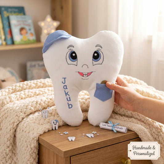 A personalized white plush tooth pillow with embroidered facial features, blue fabric accents, and the name 'Jakub' on the front, held by a hand in a cozy bedroom setting.