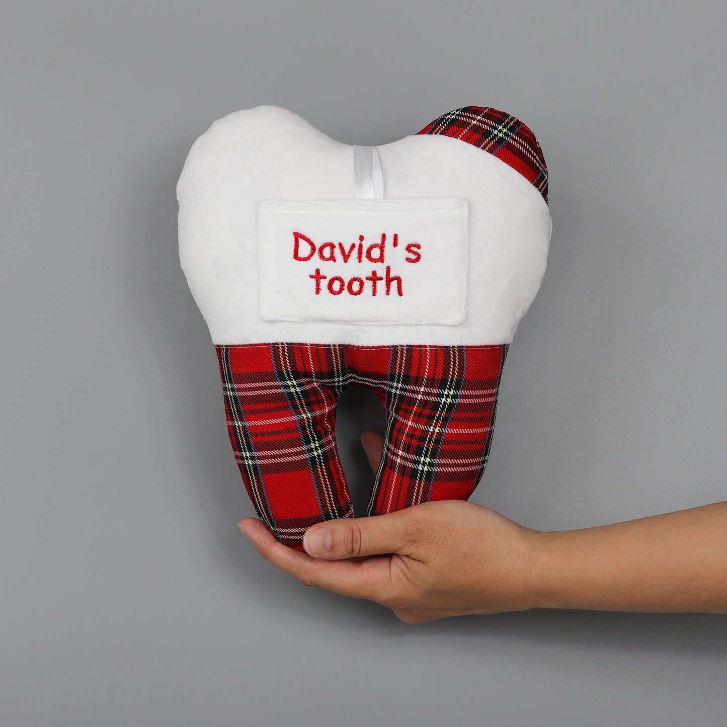 Plush tooth-shaped pillow with plaid pattern and 'David's tooth' text, held by a hand on a gray background